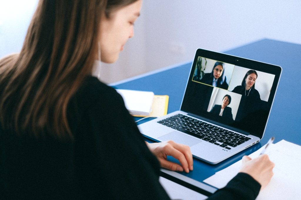 Young woman sitting in front a laptop, screen shows a video meeting in progress.